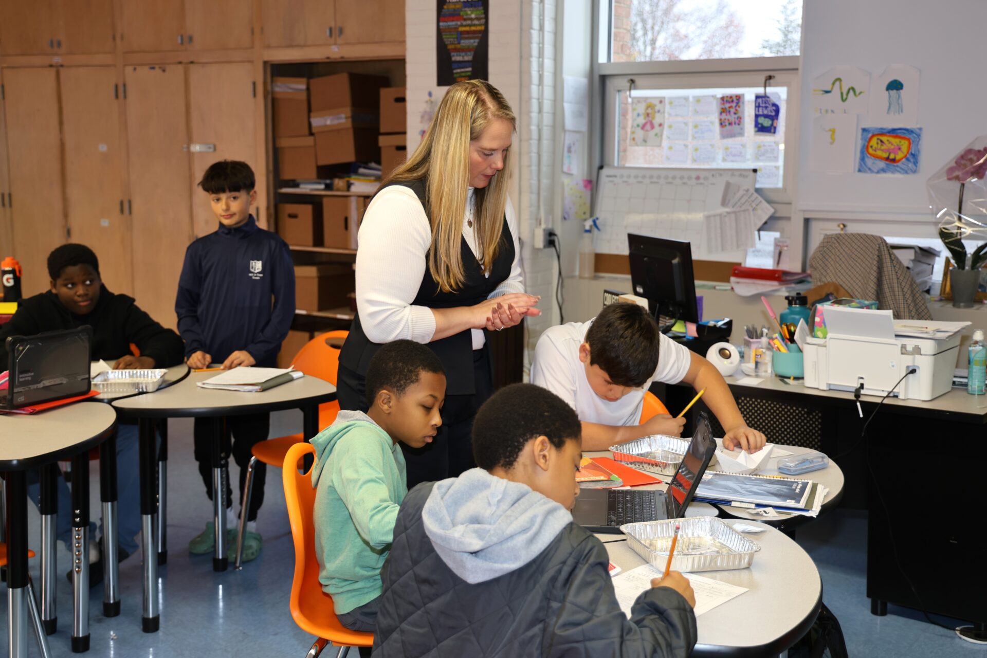 A teacher walks around students at desks in a science classroom as they work on an experiment. 