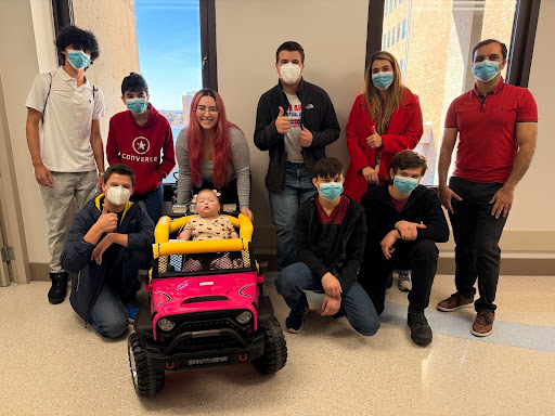 Students and teachers pose with a child in a motorized toy car.