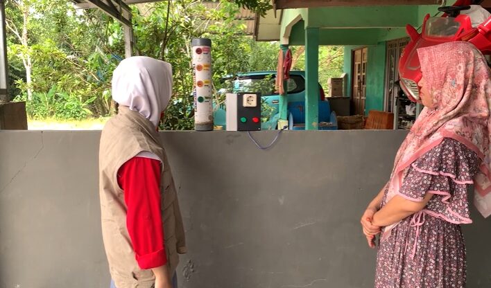 Two people turn toward the FlowSafe device sitting on a concrete ledge.