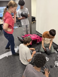 Students sit together on the floor while working with parts of a toy car.
