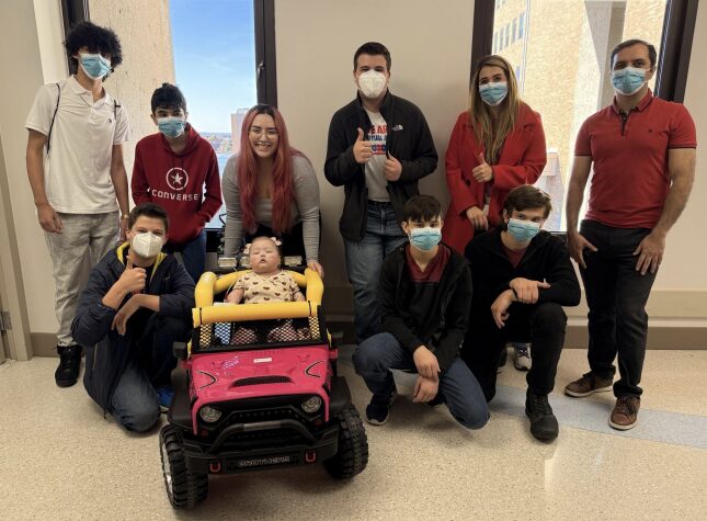 A group photo with the students, the family, and the girl in the toy car.