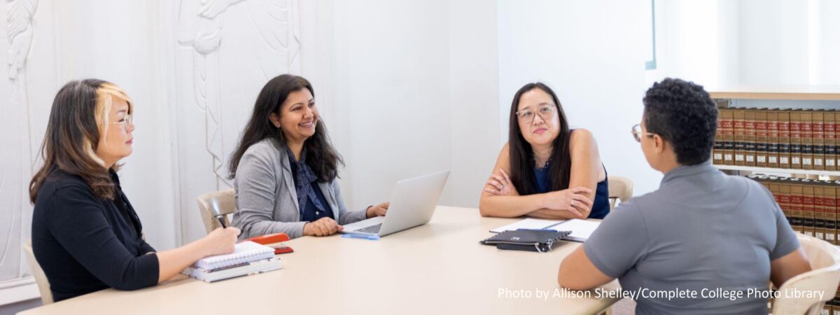 Asian and Black female faculty meeting around a table in a meeting room on a college campus.