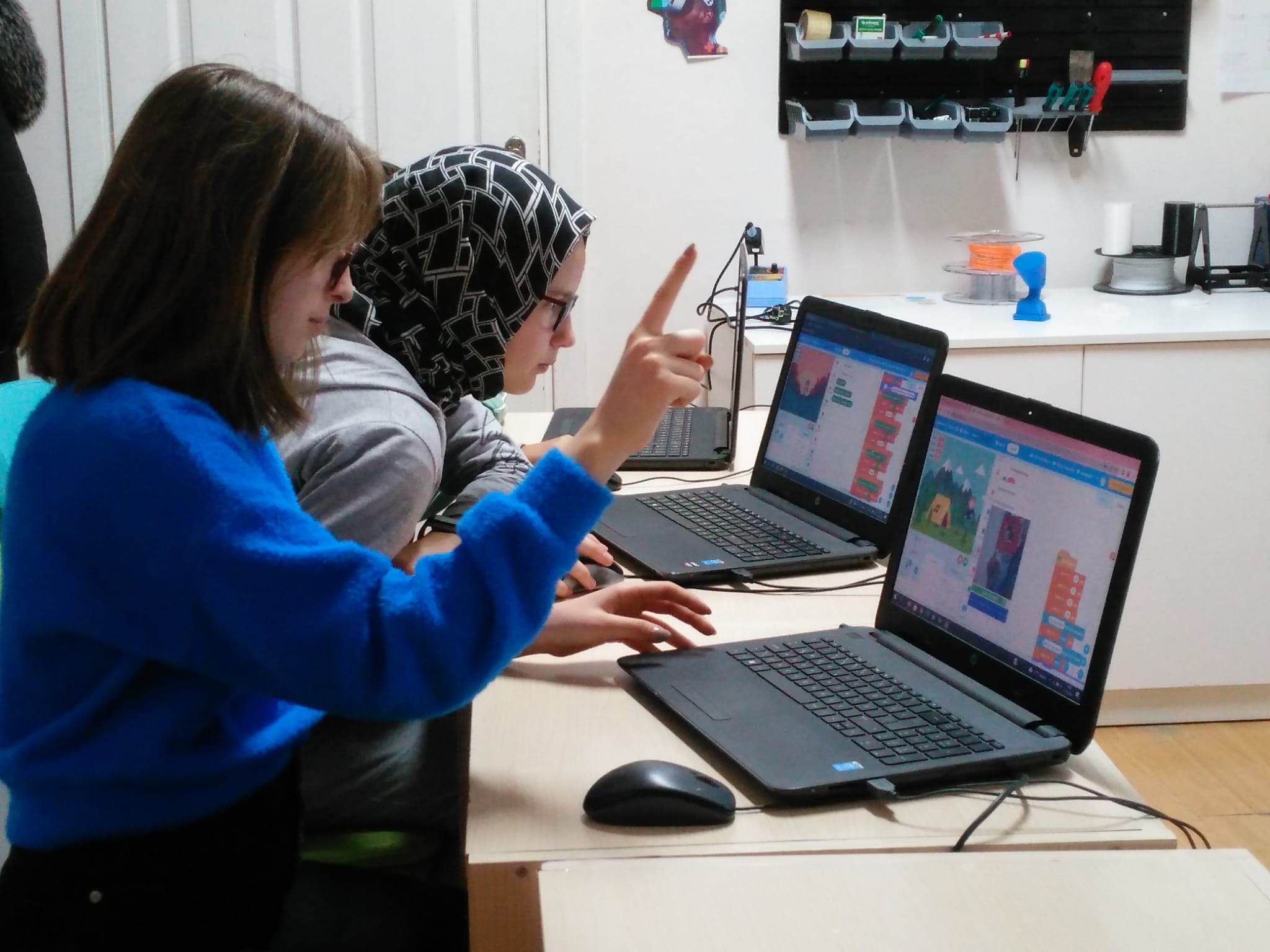 Two students work on a laptop showing coding software on the screen.