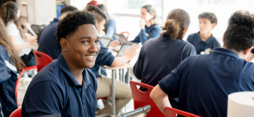 A young student smiles at the camera while sitting in a classroom