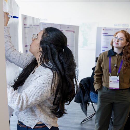 A researcher writes on a poster as another researcher watches